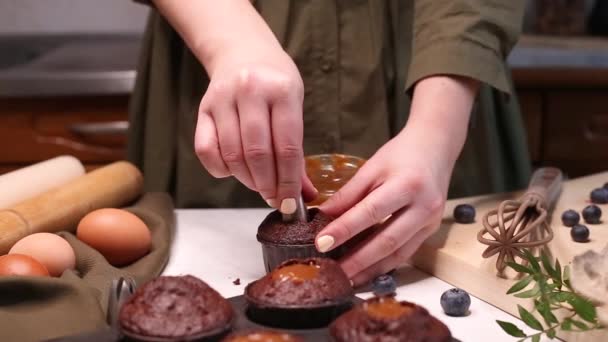 女性の手はチョコレートカップケーキにキャラメル充填を注ぎます 女性は台所でおいしいカップケーキを準備します ビデオは自家製マフィンを作る完全なプロセスを示しています — ストック動画