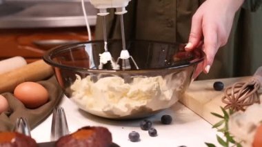 Cheesecake tatlısı için çırpılmış şeker ve kremayı peynirin içine karıştırıyorum. Bir kadın mutfakta lezzetli kekler hazırlıyor. Video, ev yapımı kek yapma sürecinin tamamını gösteriyor..