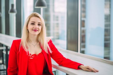 Pencerenin yanındaki açık ofis binasında kırmızı elbiseli başarılı bir iş kadını.