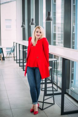Pencerenin yanındaki açık ofis binasında kırmızı elbiseli başarılı bir iş kadını.