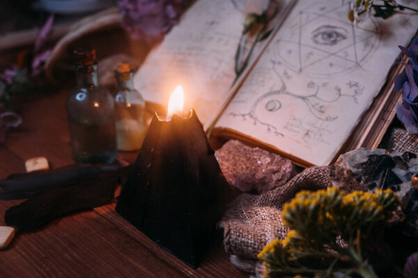Откройте старую книгу с волшебными заклинаниями, рунами, черными свечами и травами на ведьминском столе. Оккультная, эзотерическая, гадалка и викка. Хэллоуин винтажный фон