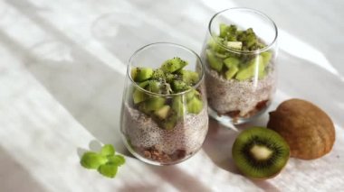 Hindistan cevizi sütüyle Chia tohumu pudingi ve granola ile bir bardakta kivi. Sağlıklı vejetaryen yemeği. Mutfakta pencereden gün ışığı, ışıltı, ışık ve parlak meyveler..
