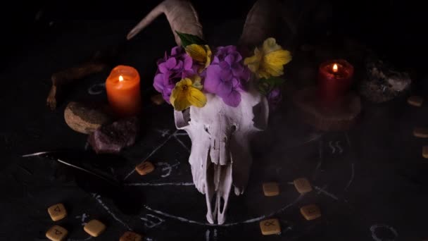 Weißer Ziegenschädel mit Hörnern, aufgeschlagenes altes Buch, Runen, schwarze Kerzen auf dem Hexentisch. Okkultes, Esoterisches, Wahrsagerisches und Zauberhaftes. Halloween-Konzept.