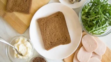 Ekmek, ricotta peyniri, jambon, roka ve ketatarla sandviç yapıyorum. Isırık ısırık tost yemek. Sağlıklı gıda konsepti. Hareket animasyonunu durdur, yukarıdan görüntüle.