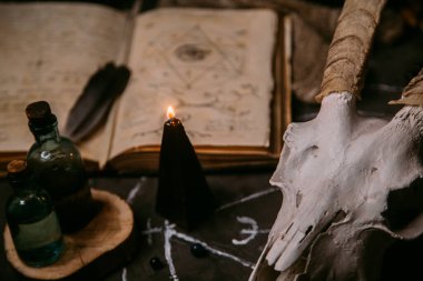 Boynuzlu beyaz keçi kafatası, açık eski kitap (metin - çevrilemez, hayali dil), cadı masasında siyah mumlar. Esrarengiz, esrarengiz, kehanet ve cadı kavramı. Cadılar Bayramı, ölüm günü konsepti
