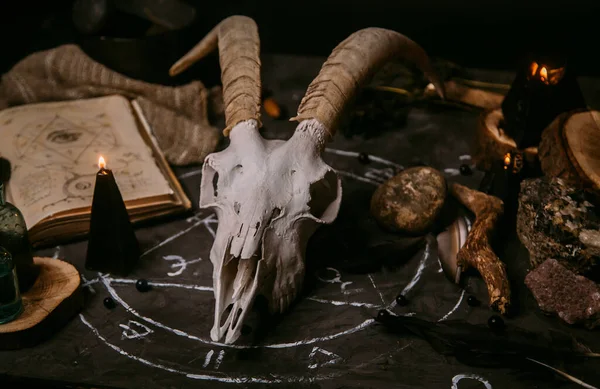 Boynuzlu beyaz keçi kafatası, açık eski kitap (metin - çevrilemez, hayali dil), cadı masasında siyah mumlar. Esrarengiz, esrarengiz, kehanet ve cadı kavramı. Cadılar Bayramı, ölüm günü konsepti