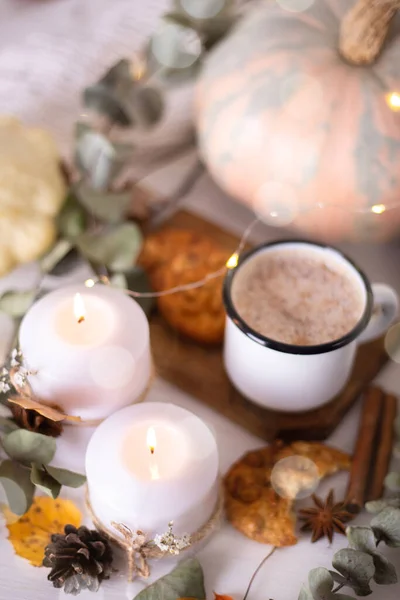 Cozy autumn composition. Hot cocoa with cookies in a white mug with white knitted scarf surrounded by autumn leaves and pumpkins on a white wooden background. Greeting card, coffee shop, Thanksgiving