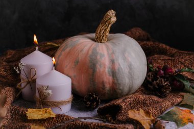 Karanlık sonbahar kompozisyonu. Mum yakan balkabakları, örgü süveter, çelenk ve kuru yapraklar. Sonbahar, sonbahar, Cadılar Bayramı konsepti