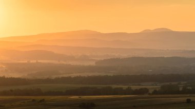 Bir dağ, sisin içinde kefen alanları üzerinde huysuz bir gün batımı.