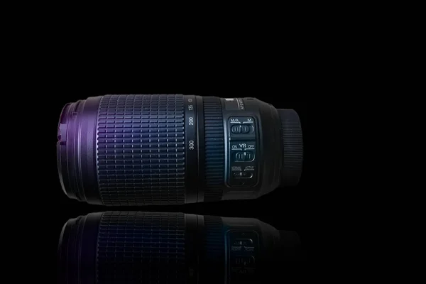Telephoto lens with image stabilization, visible zoom and focus ring. The lens is lying, side view on the black background.