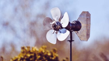 Metal levhadan yapılmış eski el yapımı yel değirmeni. Yel değirmeni bahçede duruyor ve rüzgarın yönünü gösteriyor. Gereksiz metal bir levhadan yapılmış..