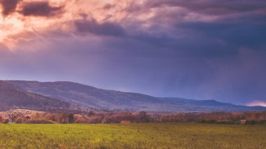 Dağların tepesinde fırtınalı bir cephe, güneş bulutların arasından doğuyor. Tarlalarda yürürken dağ tepelerinin manzarası.