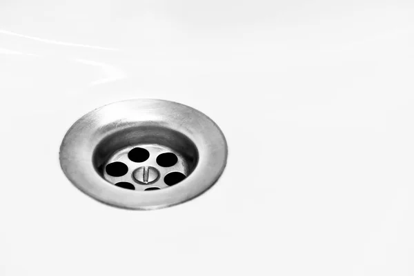 Metal bir sifonla beyaz bir banyo lavabosu, yuvarlak delikler kanalizasyon sistemine filtreleme ve su akışını kolaylaştırır..