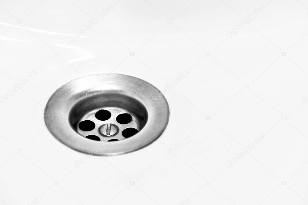 A white bathroom sink with a metal siphon, round holes facilitate filtration and drainage of water into the sewage system.