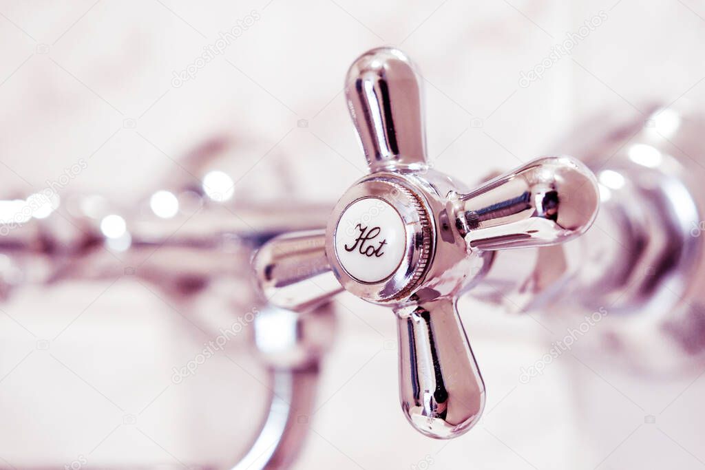 Bathroom faucet with hot water tap, made of stainless steel. The tap is attached to the tiled wall.