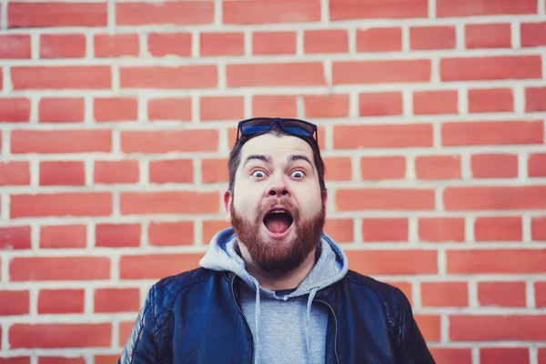 Young man opens his mouth screaming on a red brick background.