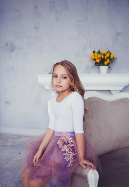 Cute little ballerina sitting on sofa in studio