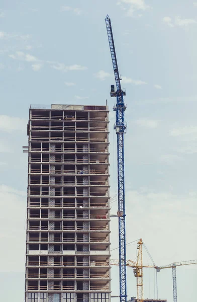 three building cranes at the background of a multi-storey buildi