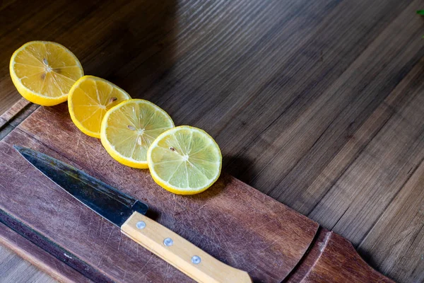 Some slices of lemon cut on a wooden board next to a knife on a rustic background