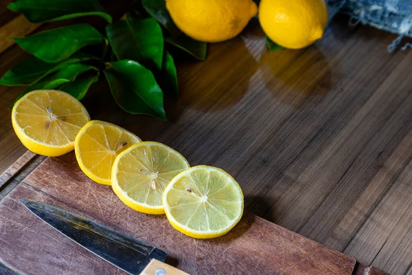 Some slices of lemon cut on a wooden board next to a knife on a rustic background