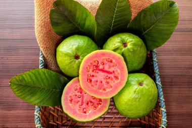 Kırsal ahşap arka planda yeşil yaprakla dilimlenmiş kırmızı guava 'ya yakın çekim.