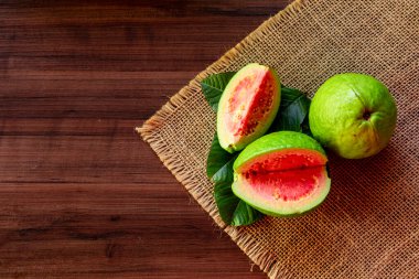 Tahta yıkım arka planında yeşil yapraklı taze kırmızı guavalar. Ağaç dokusu ve guava yaprakları...