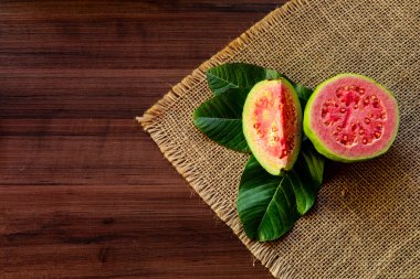 Tahta yıkım arka planında yeşil yapraklı taze kırmızı guavalar. Ağaç dokusu ve guava yaprakları...
