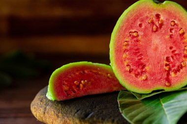 Tahta yıkım arka planında yeşil yapraklı taze kırmızı guavalar. Ağaç dokusu ve guava yaprakları...