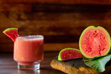 Lezzetli kırmızı guava suyu bir dilim guava yanında, arka planda guava ve kırsal ahşap yapraklar.