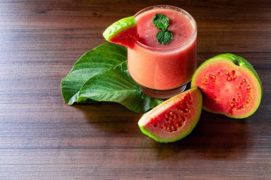 Lezzetli kırmızı guava suyu bir dilim guava yanında, arka planda guava ve kırsal ahşap yapraklar.