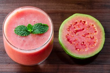 Lezzetli kırmızı guava suyu bir dilim guava yanında, arka planda guava ve kırsal ahşap yapraklar.