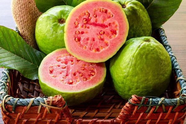 Kırsal ahşap arka planda yeşil yaprakla dilimlenmiş kırmızı guava 'ya yakın çekim.