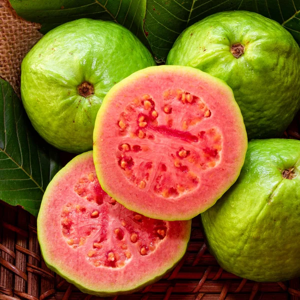 Kırsal ahşap arka planda yeşil yaprakla dilimlenmiş kırmızı guava 'ya yakın çekim.