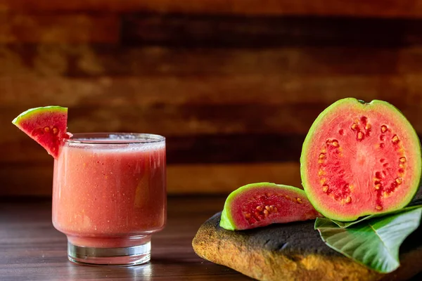 Lezzetli kırmızı guava suyu bir dilim guava yanında, arka planda guava ve kırsal ahşap yapraklar.