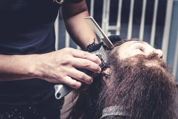 Barber using shaver to cut beard of a man .