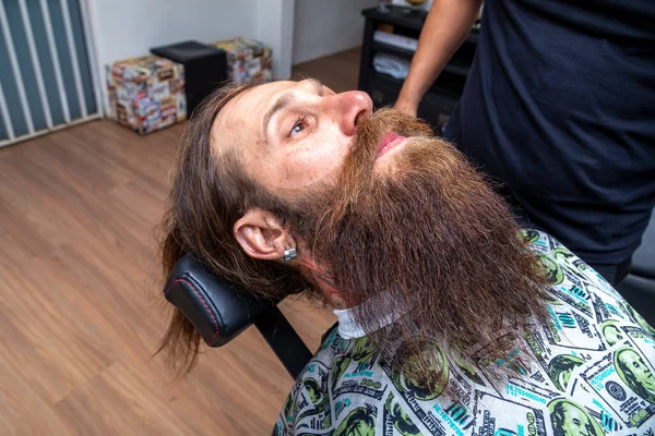 红头发的男人坐在理发店的椅子上炫耀他那漂亮的修剪过的胡子 — 图库照片