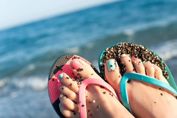 女性足スリッパ夏ペブルビーチで複数の色のペディキュア 青い海の絵の背景を持つ活気に満ちた屋外水平感動クローズ アップ画像 — ストック写真
