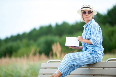 Genç ve güzel kadın yaz şapka ve güneş gözlüğü kitap okuma. Açık havada yakın çekim yatay renkli görüntü