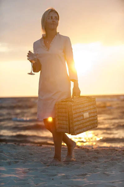 壮大な夕日を背景に海辺の砂の上を歩いてビーチにワイングラスを持つ女性の笑みを浮かべてください 夏屋外クローズ アップ垂直色イメージ — ストック写真