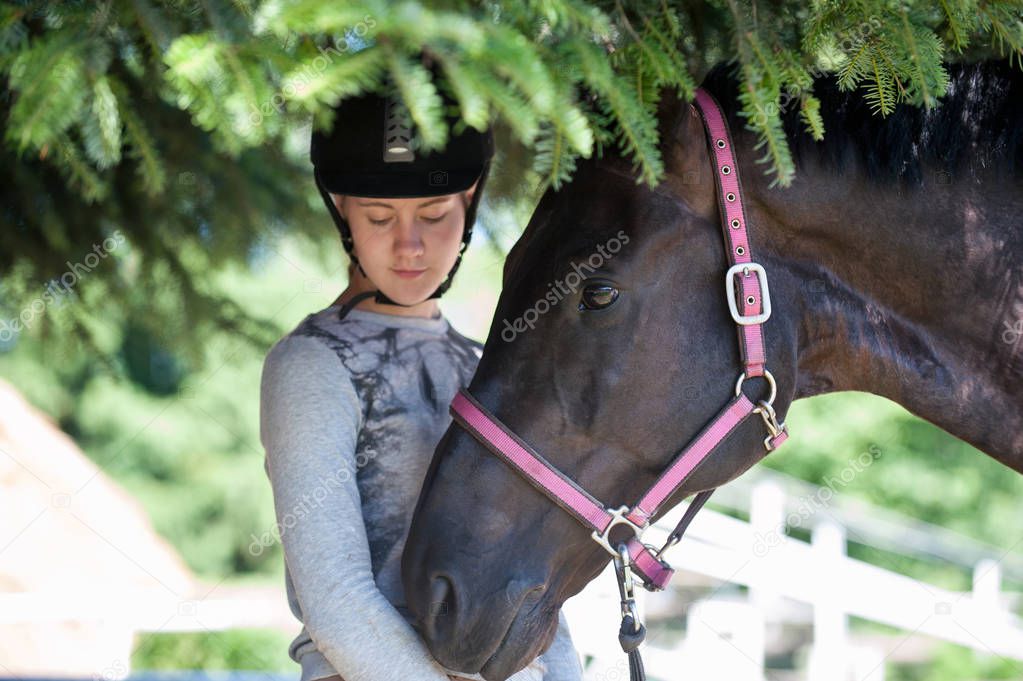 Portrait of chestnut horse head together with her owner-young teenage girl equestrian. Colored outdoors horizontal summertime image.