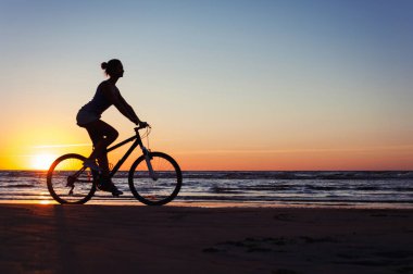 Sportif kadın binicilik bisiklet çok renkli Sunset'teki silüeti