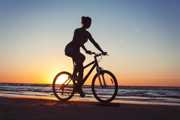 Silhouette of sporty woman riding bicycle on multicolored sunset — Stock Photo, Image