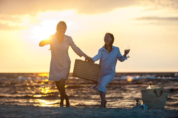 Две молодые женщины веселятся и пьют белое вино на берегу моря — стоковое фото
