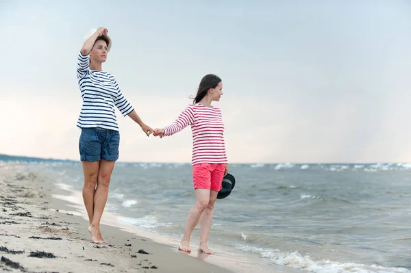 Två unga kvinnor som går tillsammans håller händerna på havet — Stockfoto