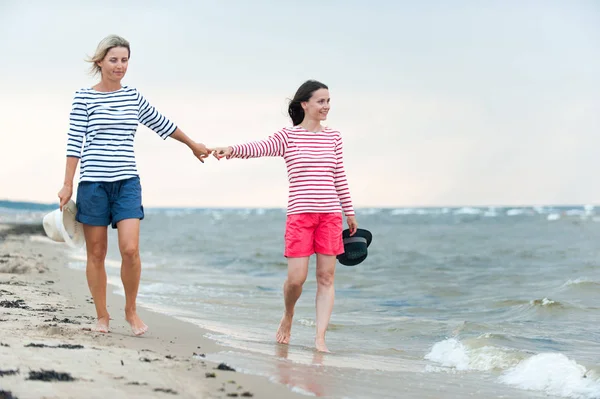 海辺で手をつないで一緒に歩く二人の若い女性 — ストック写真