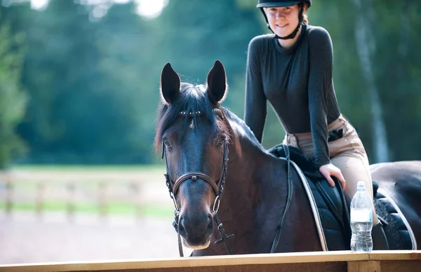 Young pretty girl resting after horse riding training on arena — Stock Photo, Image