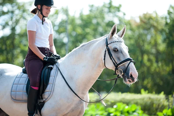 Joven bonita chica cabalgando caballo blanco en verde parque fondo — Foto de Stock