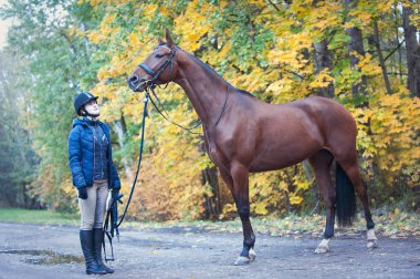 Genç bayan binici kestane ağaçlarının yanında duruyor.