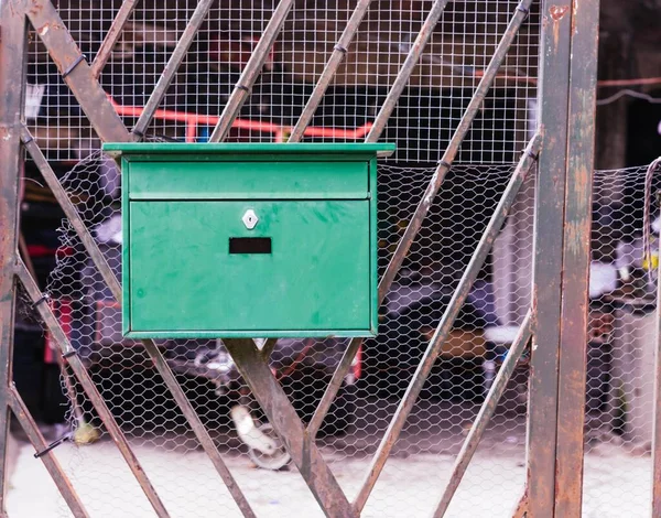 A retro looking green mailbox, or mailbox, attached to the metal fence