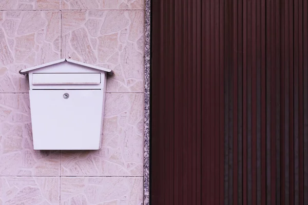 A retro-looking white mailbox, or letterbox, taped to the white exterior wall